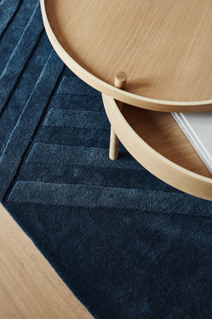 The interior design trends of spring 2023 offer an interior rich in contrasts, where this striped blue wool rug from NJRD is a nice contrast to the round wooden table from Menu.