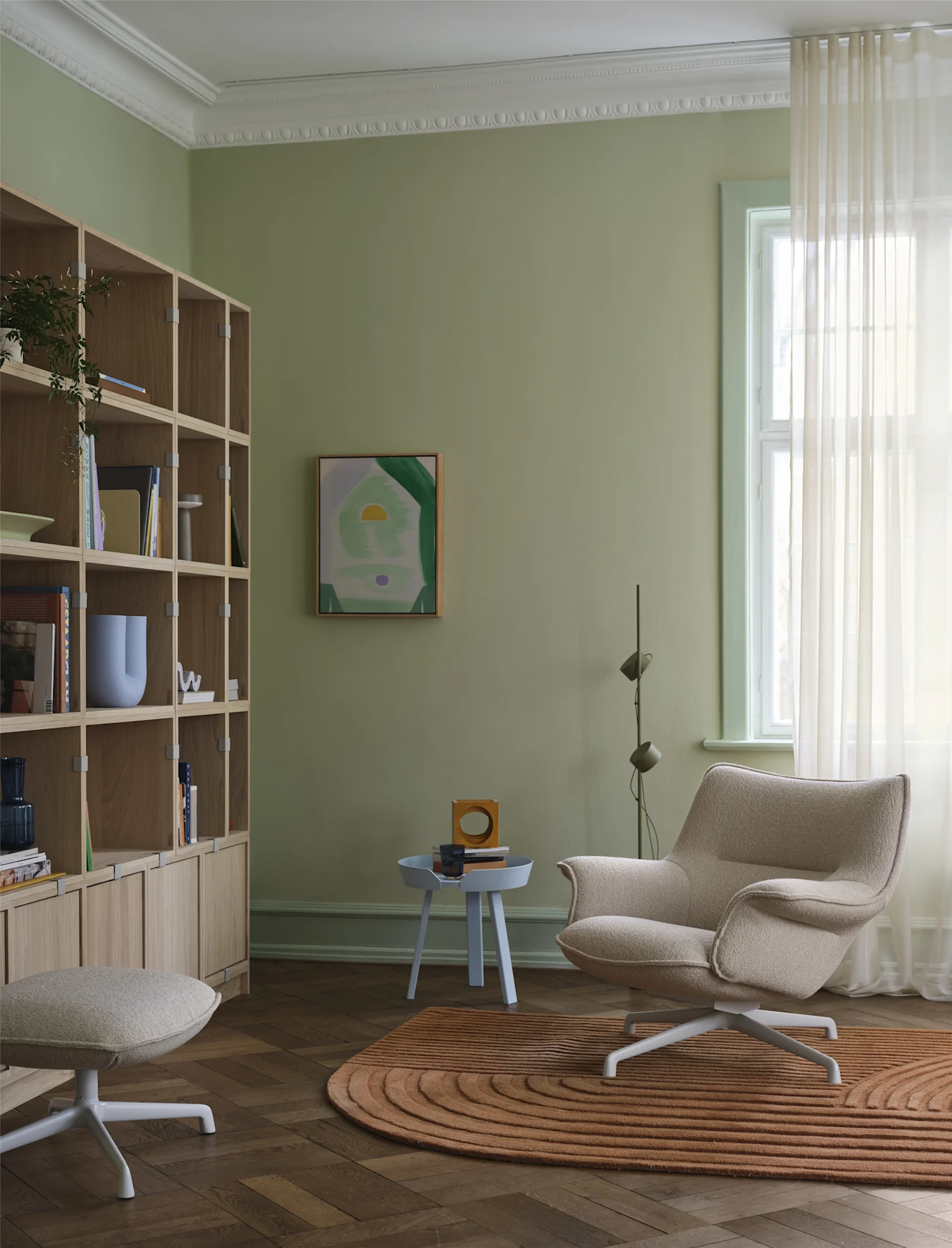 The beige-coloured Doze armchair from Muuto stands in front of a bookshelf in a cosily furnished living room.