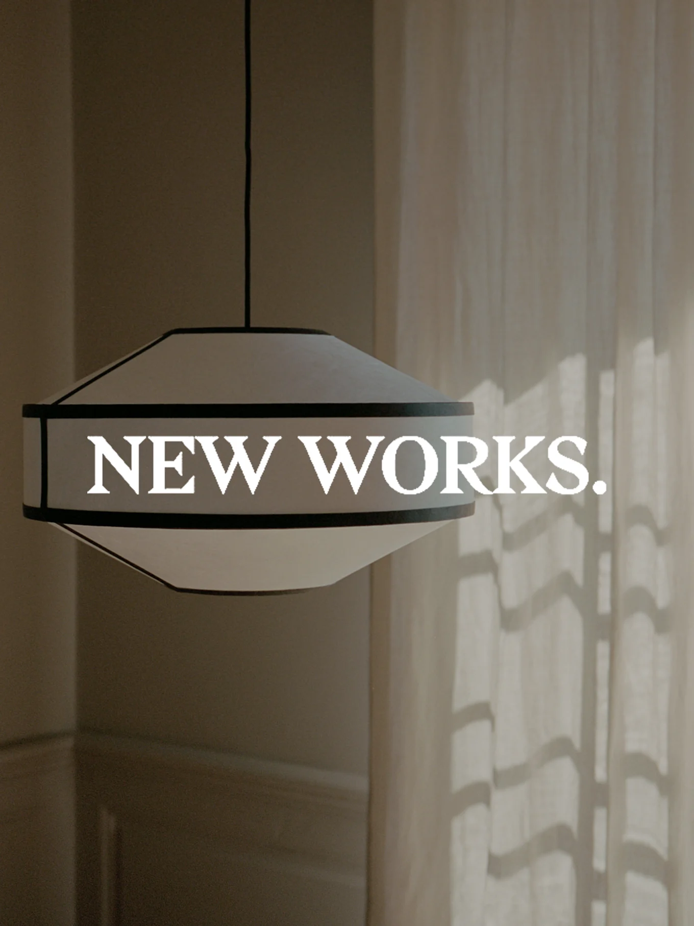 A wide, white and dark-rimmed pendant light fixture hangs, with 'NEW WORKS.' text overlaid. Sunlight casts shadows on a curtain.