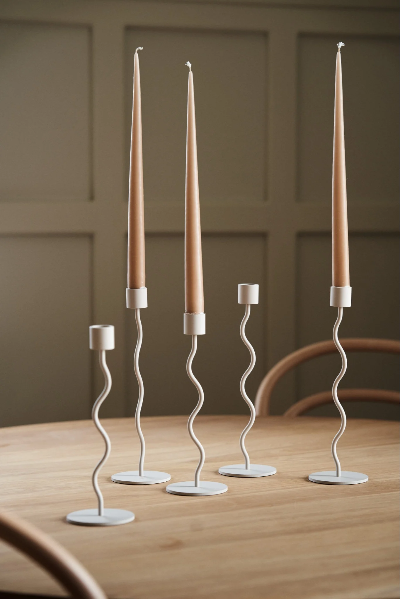 A collection of the Curve candle holders in beige from Cooee Design on a wooden dining table.