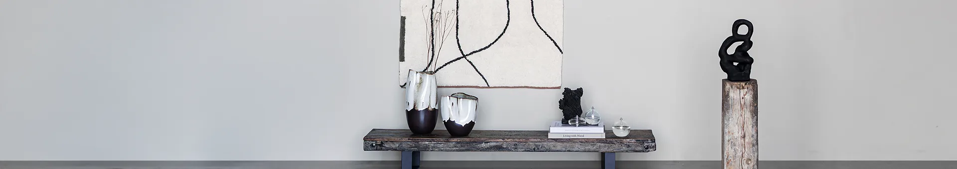 Modern interior with abstract art, two brown and white vases on a rustic bench, and a black abstract sculpture on a pedestal.