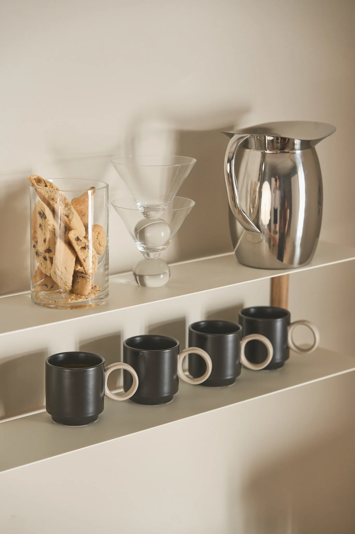 The Nivo shelf from Gejst is perfect for your coffee bar at home. Here you can see it filled with a glass of biscotti, several Noor cups from Byon and the Indian Steel jug from Hay.