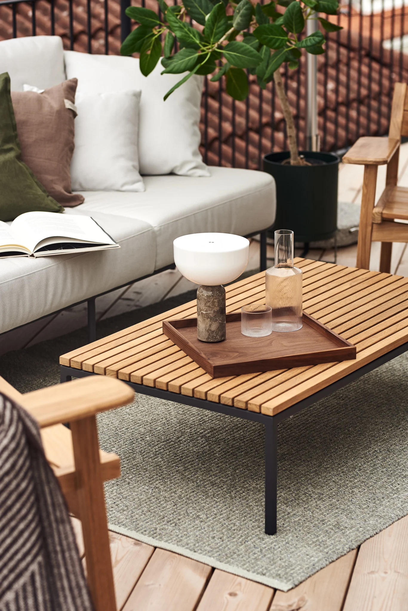 The Kizu table lamp and a Ripple carafe stand on an outdoor table on a balcony.