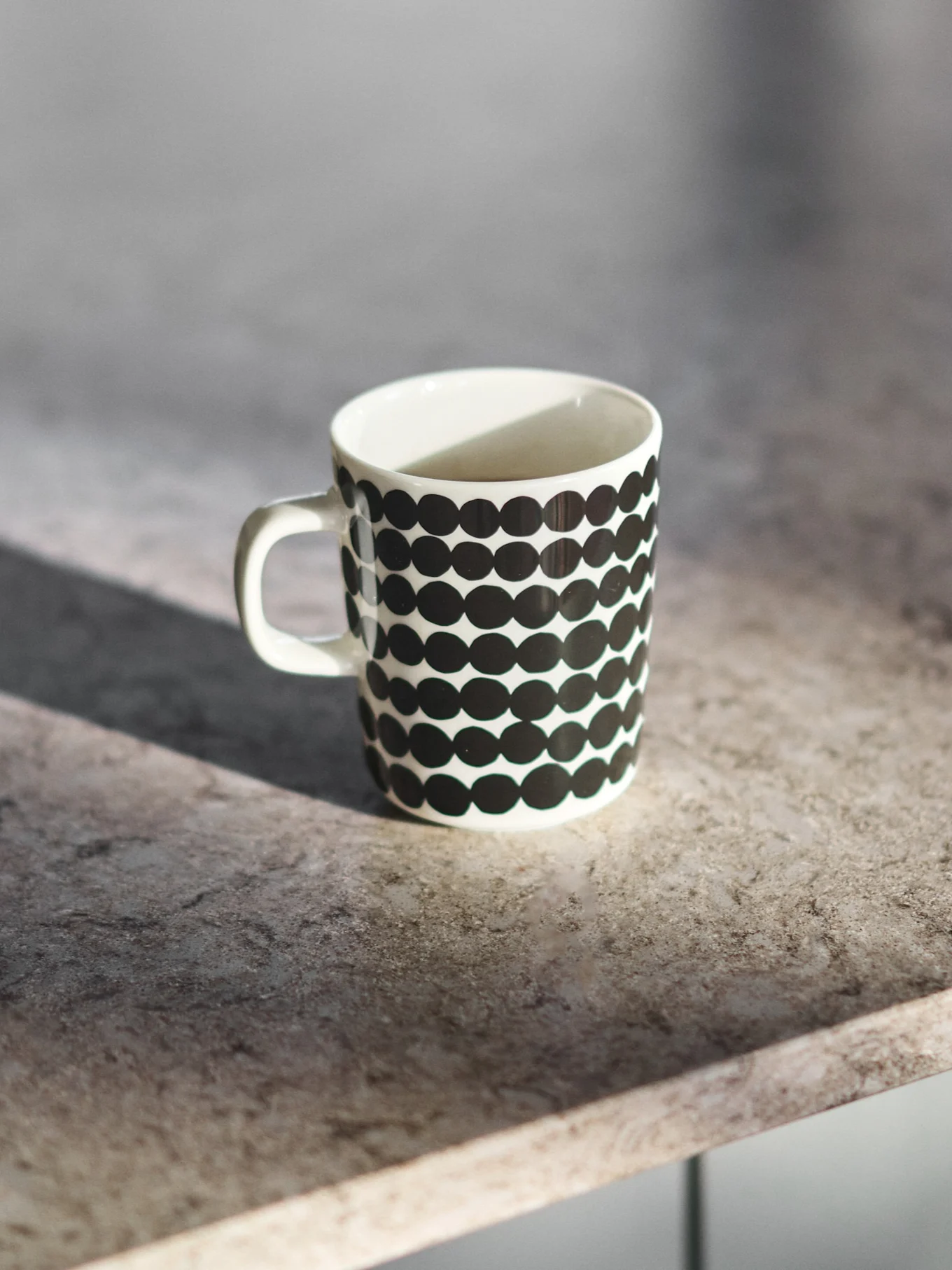 White ceramic mug with black polka dots on a grey countertop.