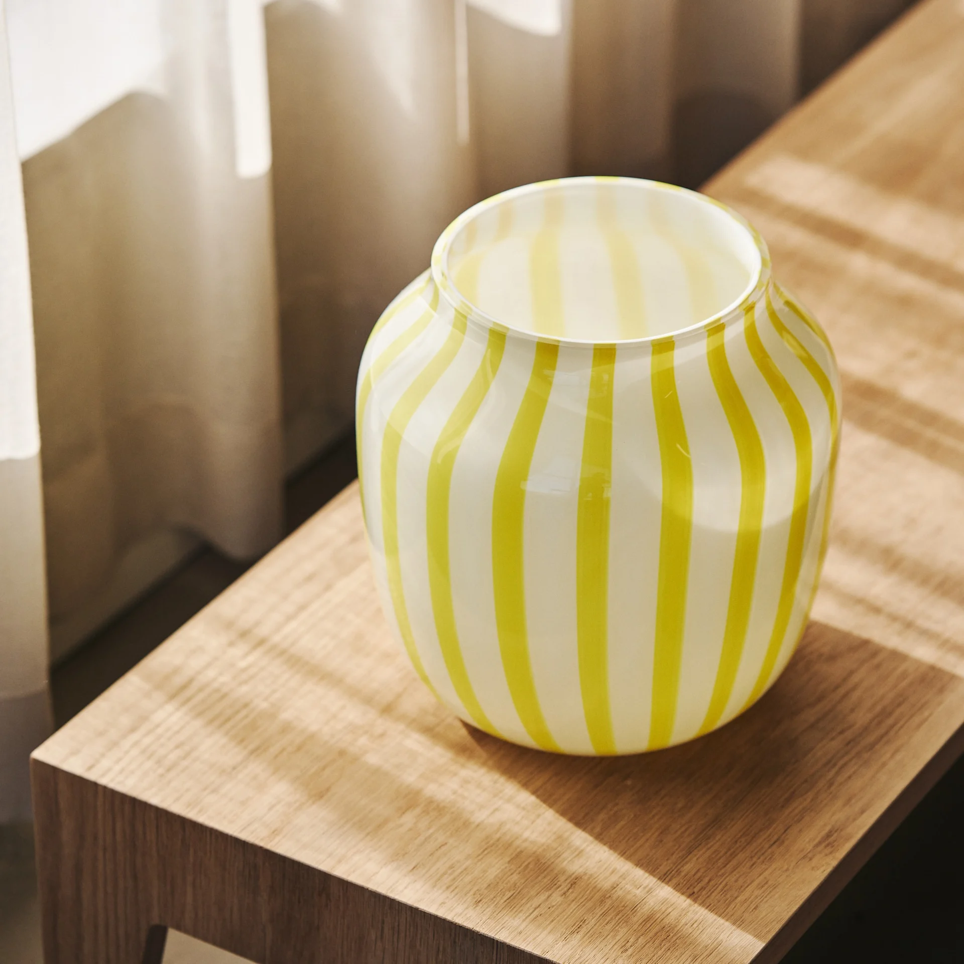 Round glass vase with vertical yellow and white stripes on a wooden surface.