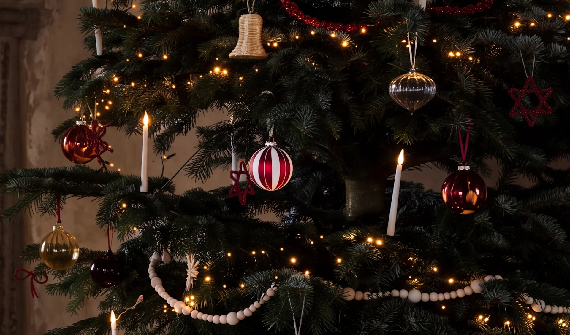 A decorated Christmas tree with warm lights, red, silver, and gold baubles, white candles, and wooden bead garlands.