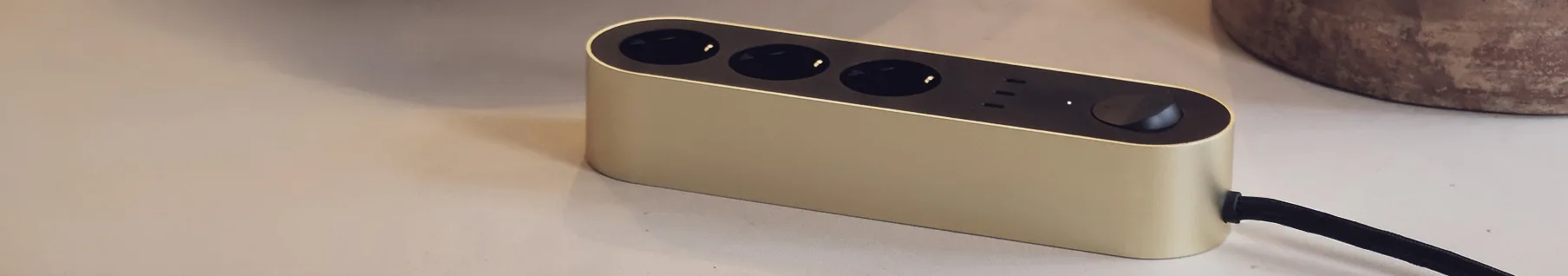 Gold power strip with three black outlets and a power button on a light surface.