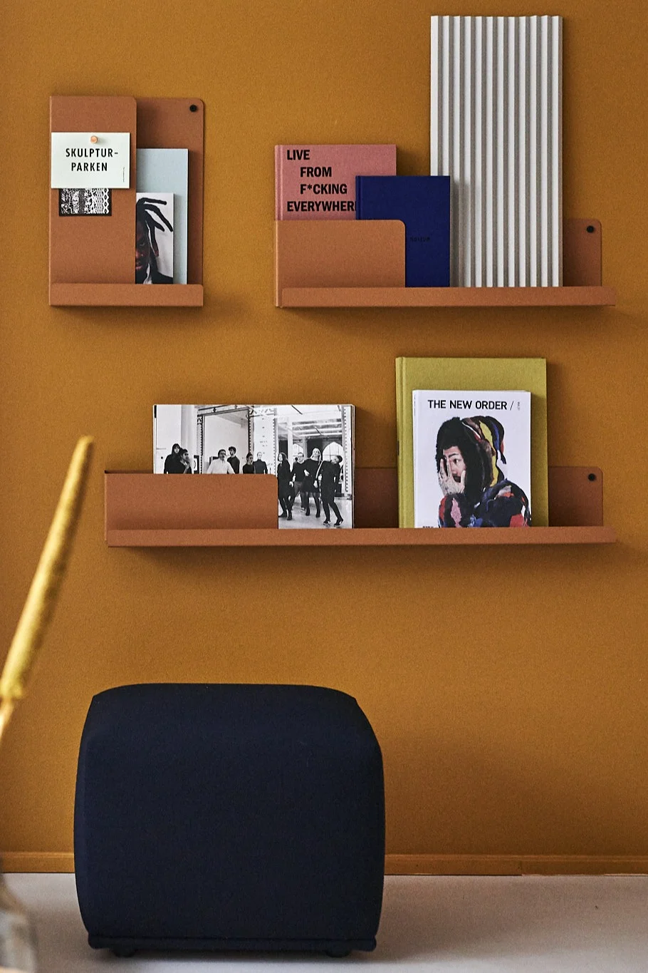 Burnt orange folded shelves from Muuto against a burnt orange wall with dark blue sit pouf. 