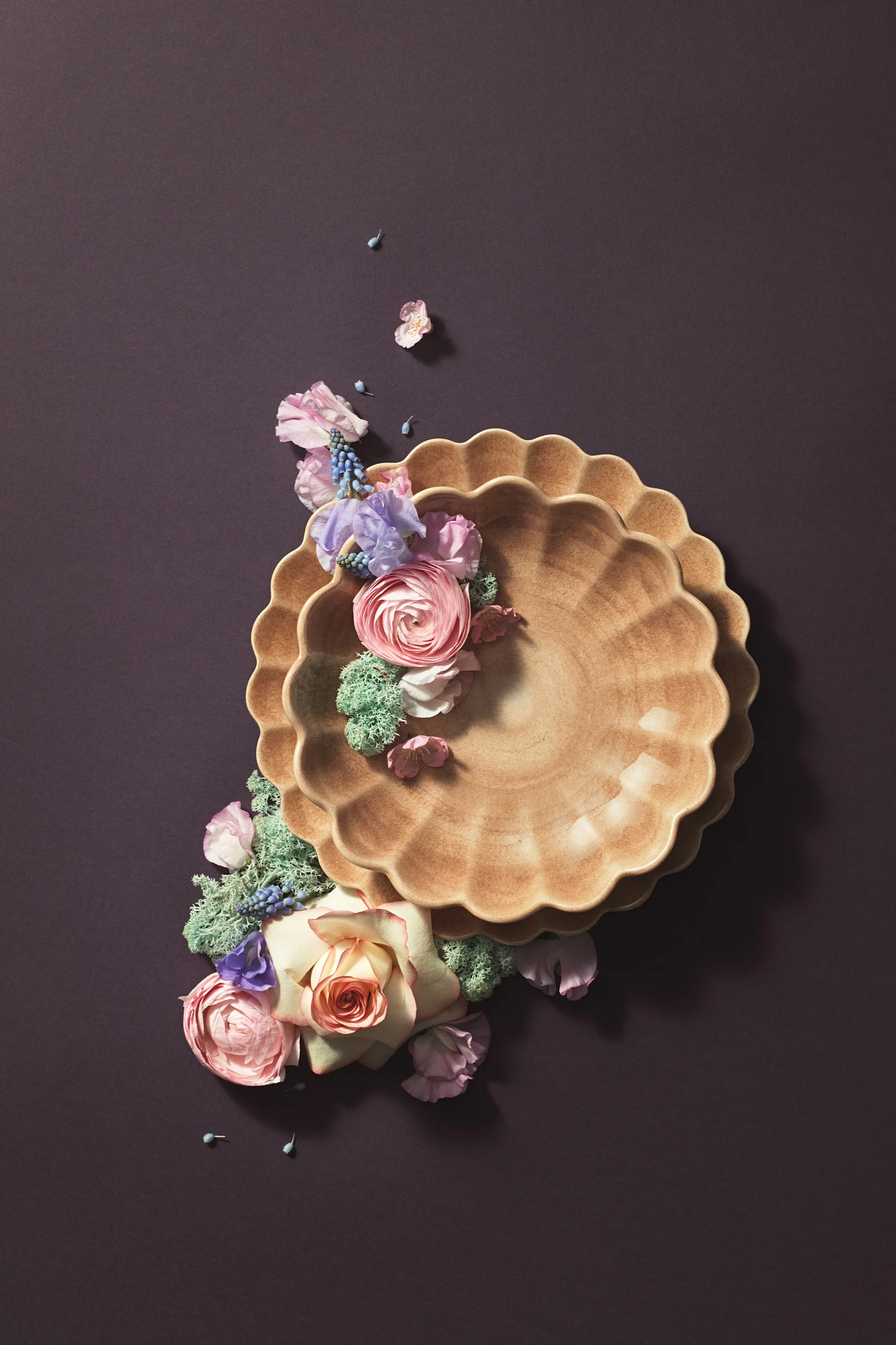 A plate and a bowl from the Oyster collection in the colour Cinnamon by Mateus have been artfully staged with flowers against a brown background.