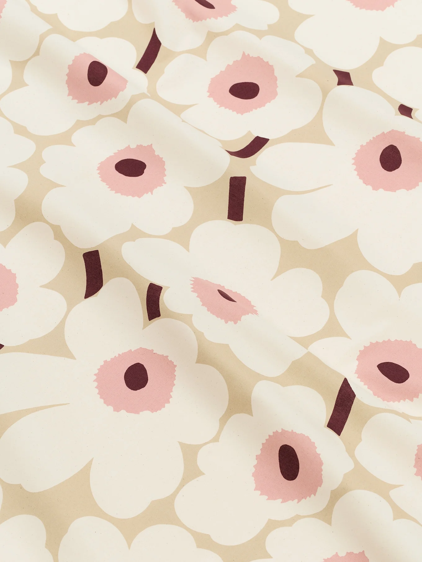 A close-up of a light beige fabric patterned with large white stylized flowers with pink centers and dark burgundy stems.