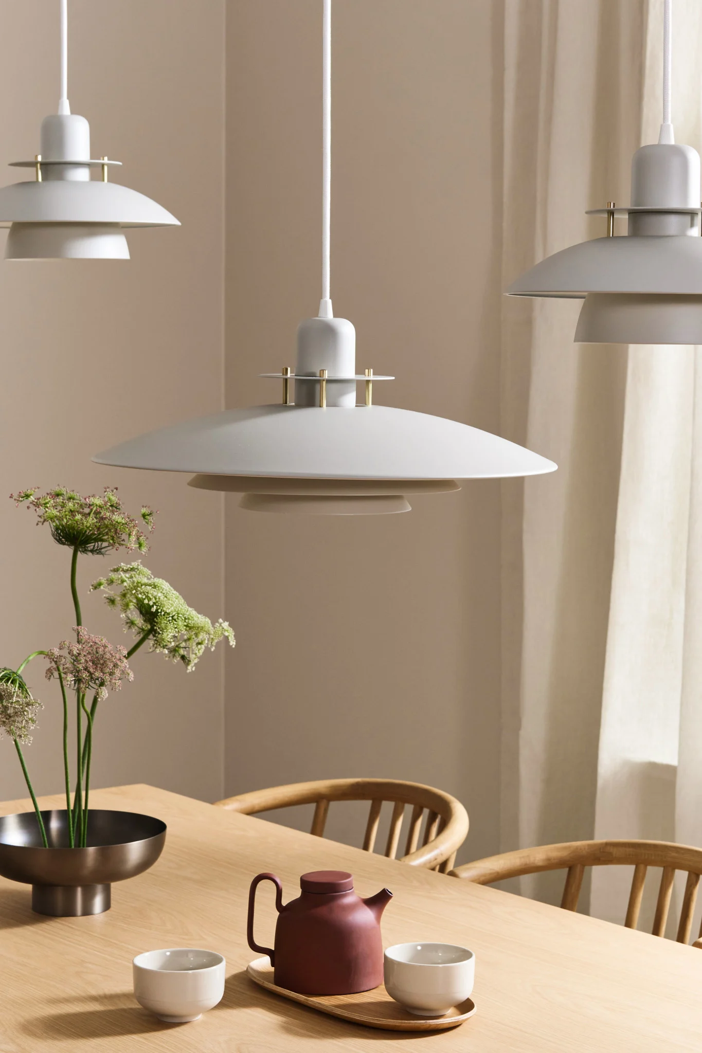 Three white Priums lamps from Belid hanging over an oak dining table in Japandi style.