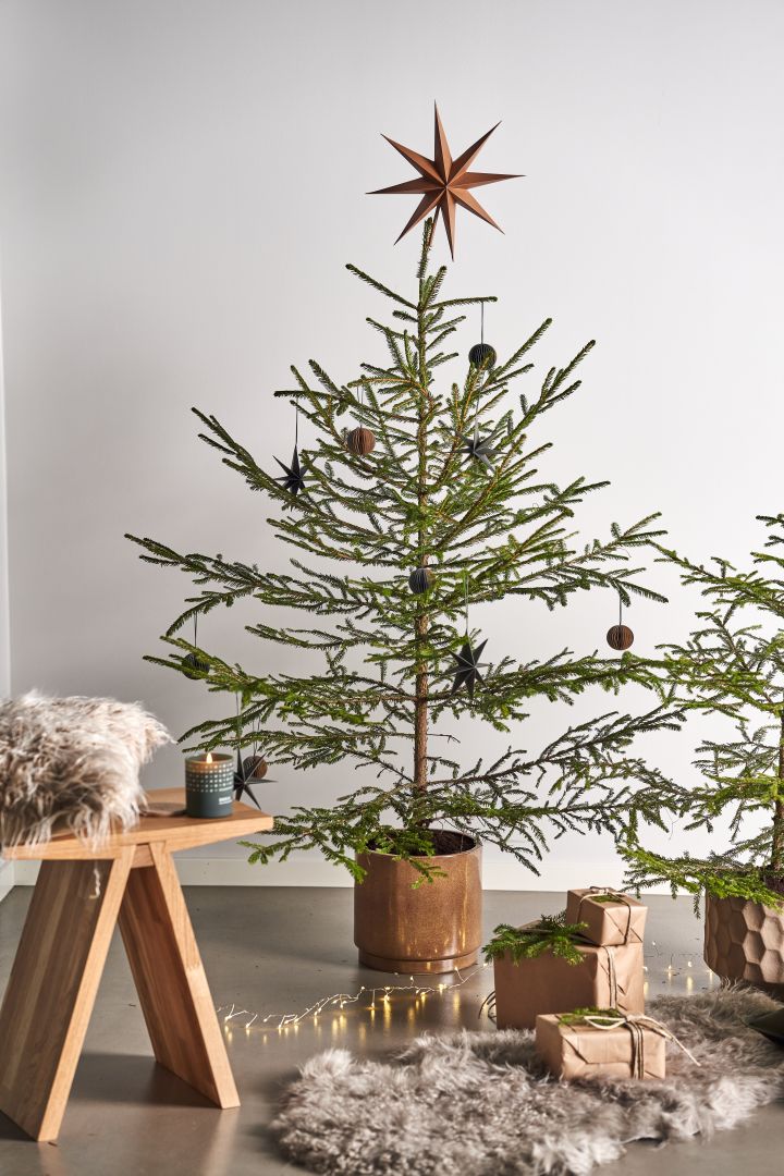Decorate the Christmas tree with Christmas tree decorations for 2021 in 4 different styles according to Nest Trends - Nurture, Share, Boost and Cultivate. Here you see Angle stool from Muubs with A Skandinavisk scented candle in the Forest scent next to packages on a sheepskin rug. 