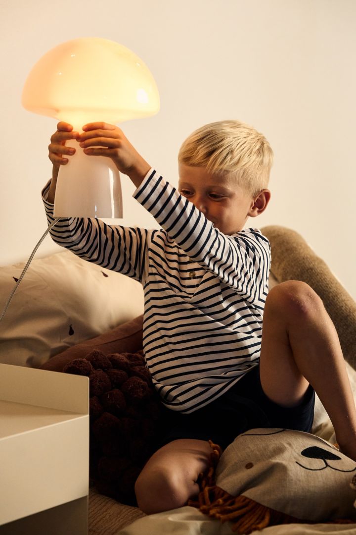 Here you see a child holding the mushroom table lamp Fungo from Globen Lighting. 