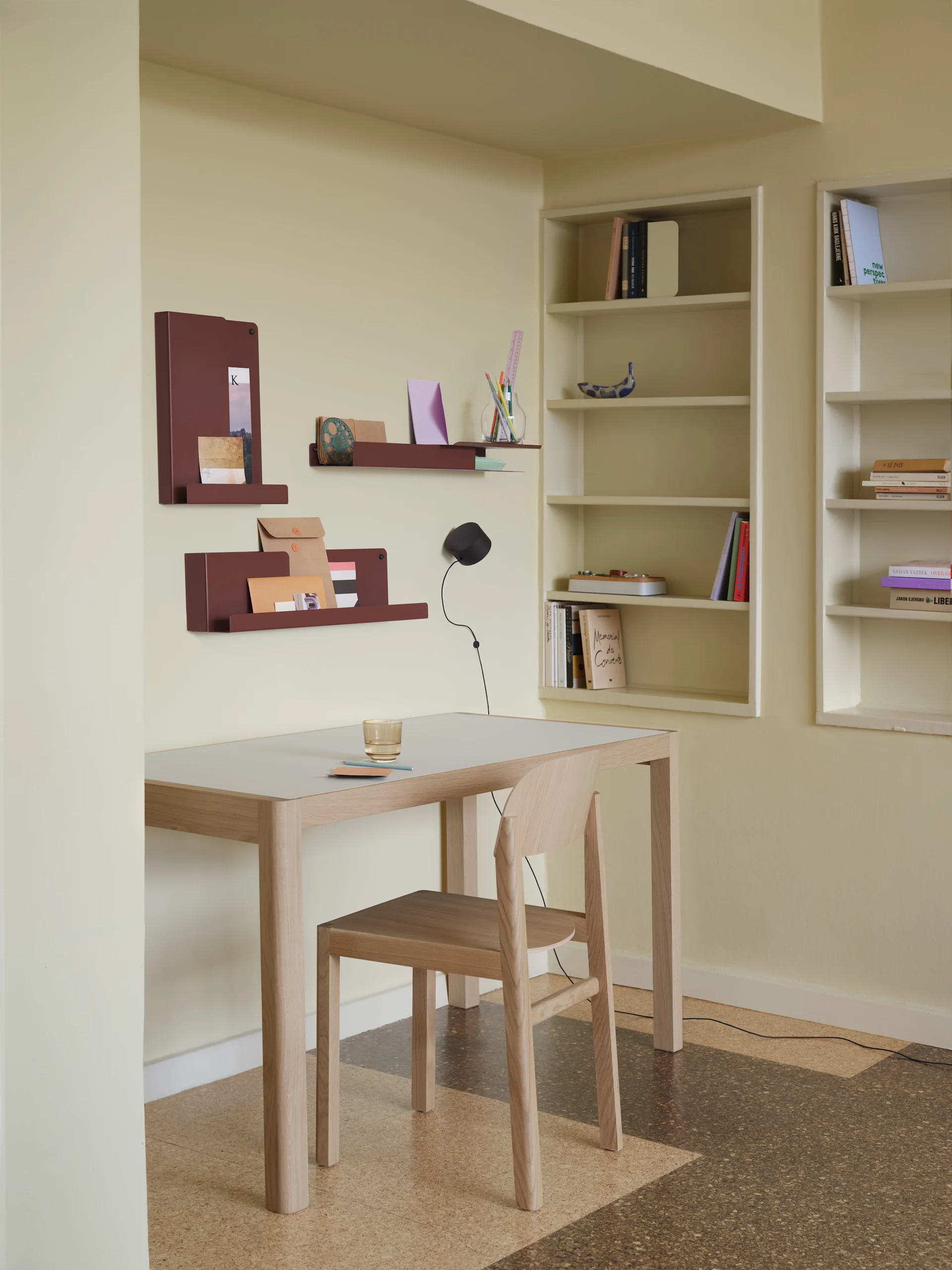 A minimalist office setup with a light wood desk, chair, reddish-brown wall organizers, and built-in bookshelves.