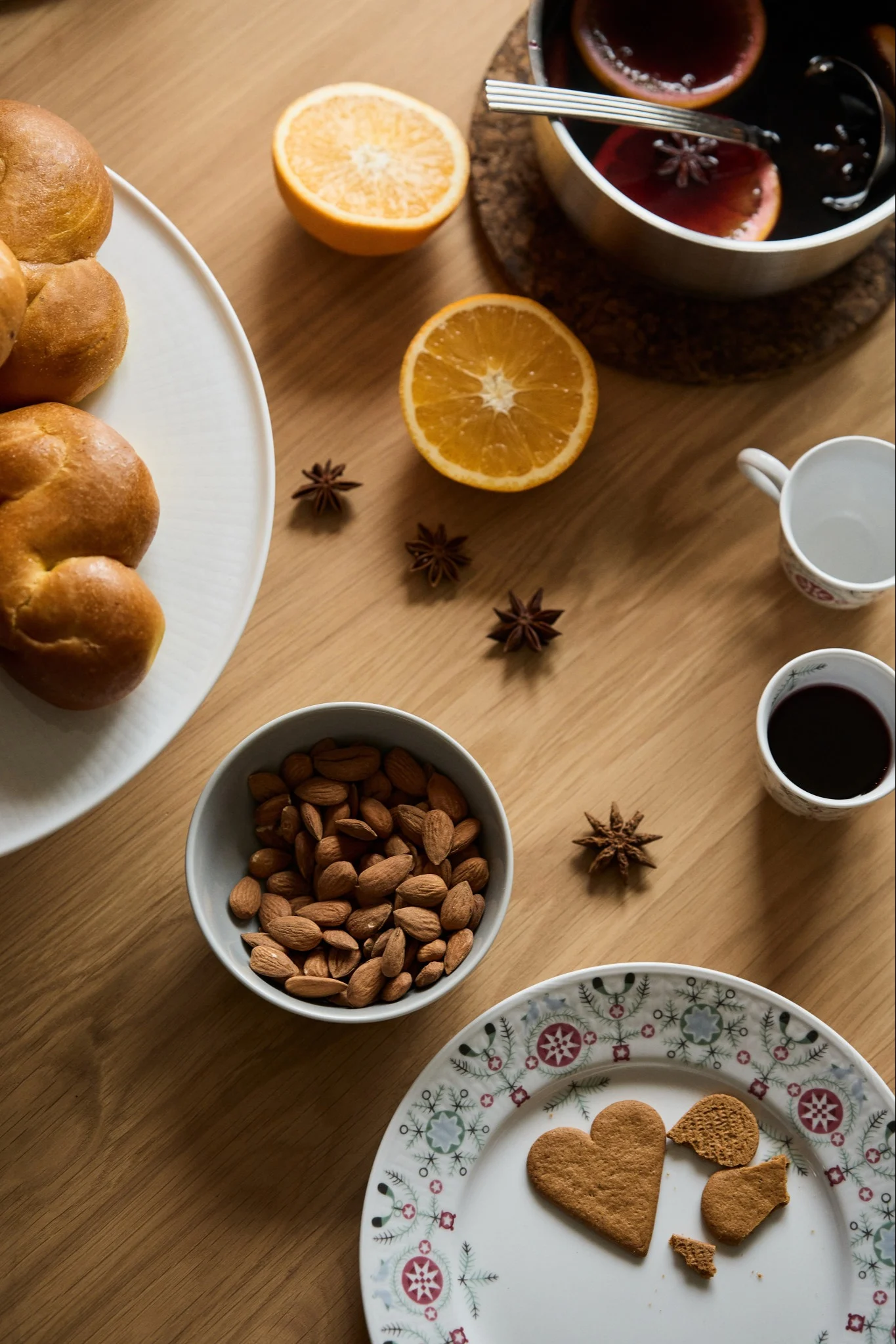 Mulled wine with orange slices, almonds, gingerbread, Lussebullar and star anise are placed on a wooden table to celebrate the first Sunday of Advent. 