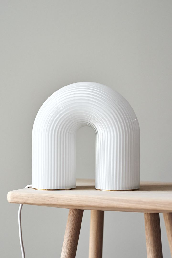 Refresh your home with modern lighting - here you see a playful Ferm Living Vuelta table lamp in white on a small wooden stool.