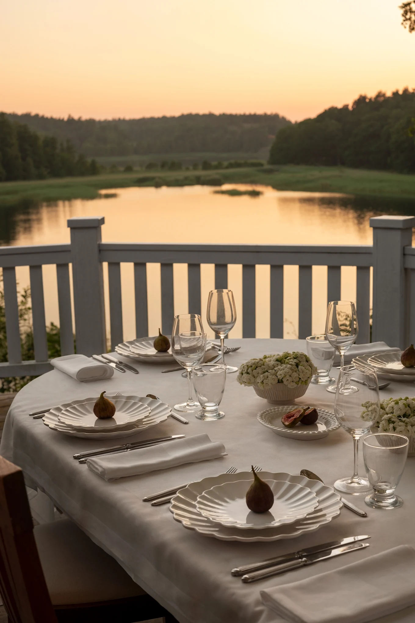 A table at sunset on a terrace overlooking a lake. The table is set in white with plates from the Oyster collection by Mateus.
