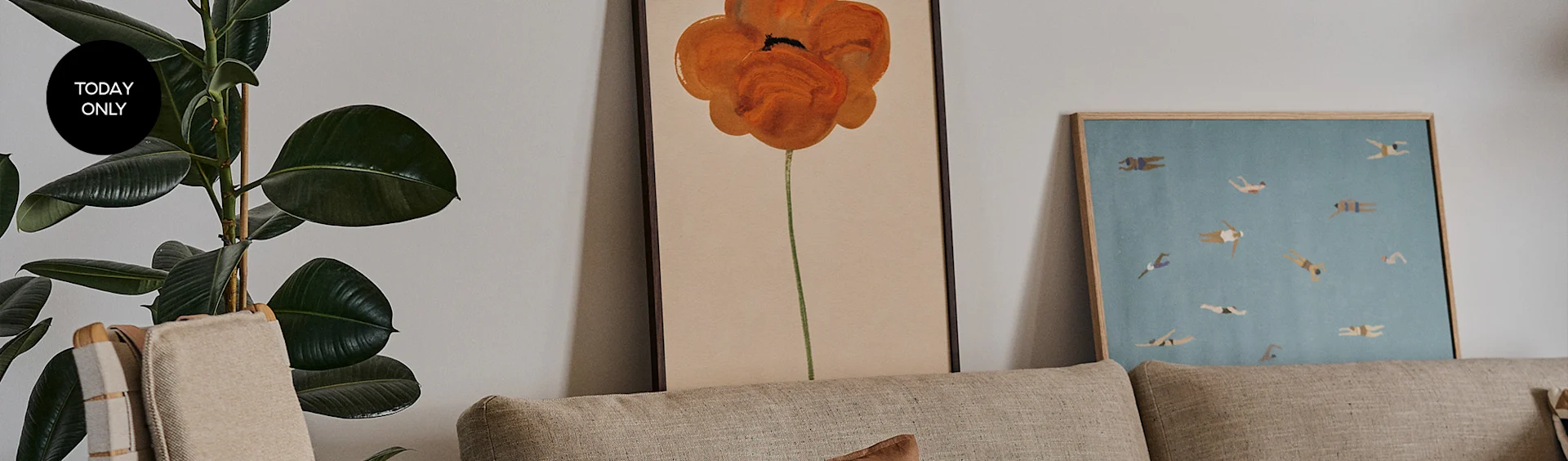 A houseplant with a "Today Only" tag next to framed art of an orange poppy and swimmers, behind a beige sofa.