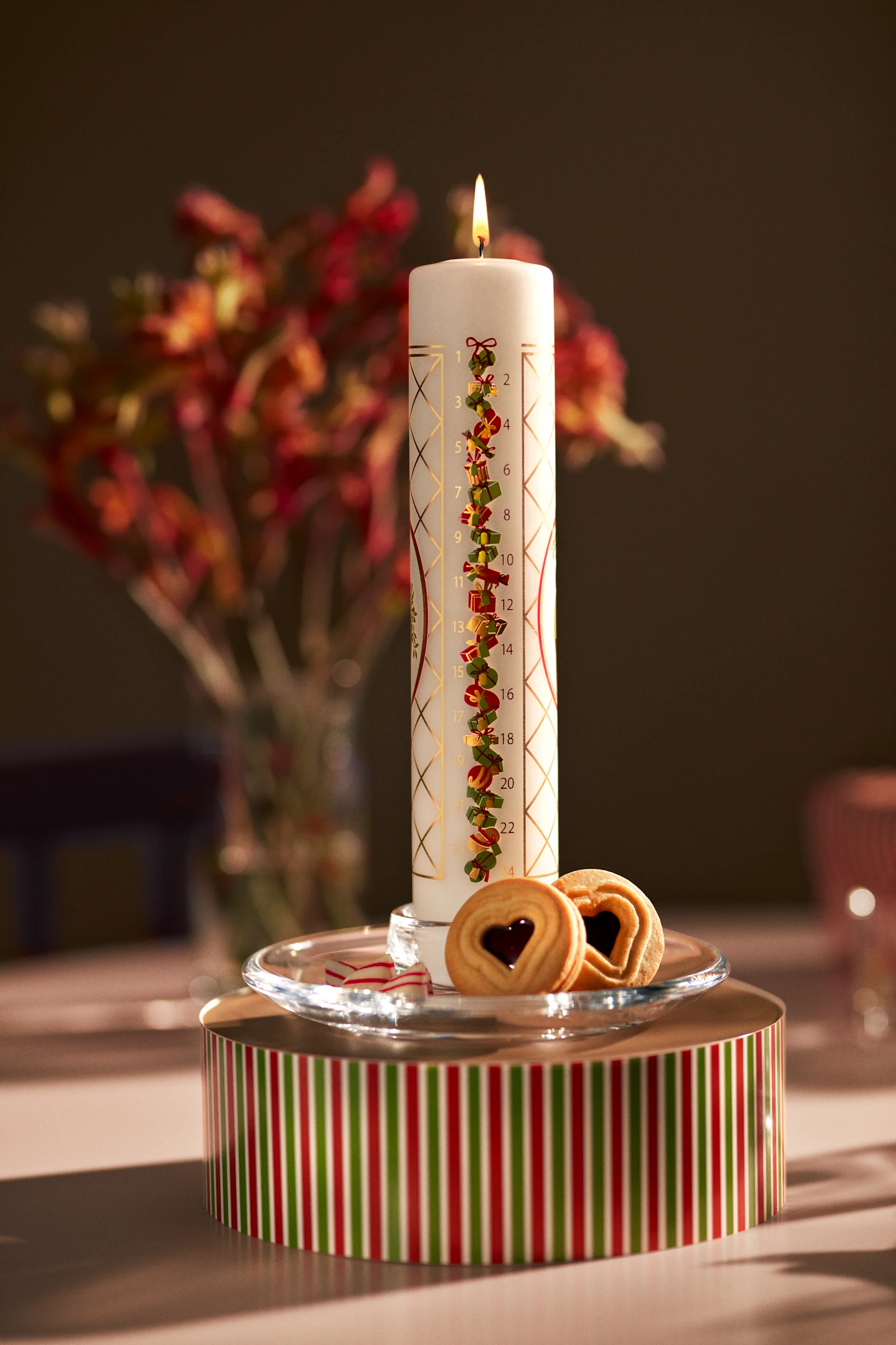 The Holmegaard Advent candle stands on a festive box, together with biscuits.