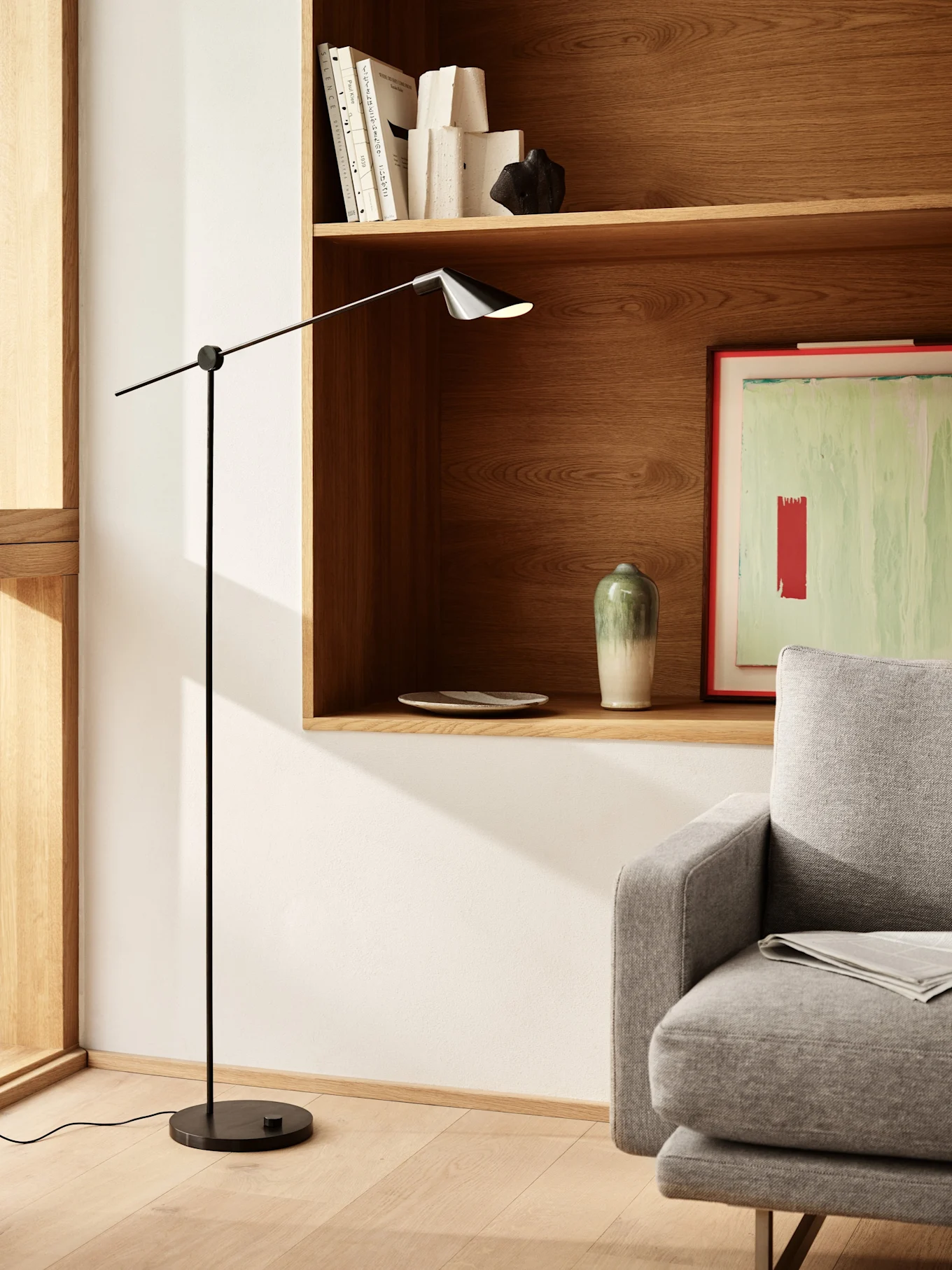A modern living room with a sleek black floor lamp, wooden shelves holding books and decor, and part of a gray sofa.