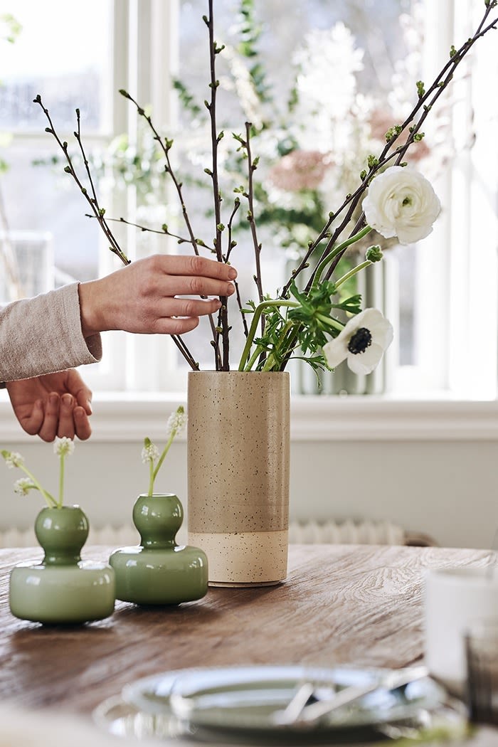Stylish Easter decorations do not have to be traditional but can be minimalistic like here with a rustic vase and smaller vases in green filled with spring flowers.