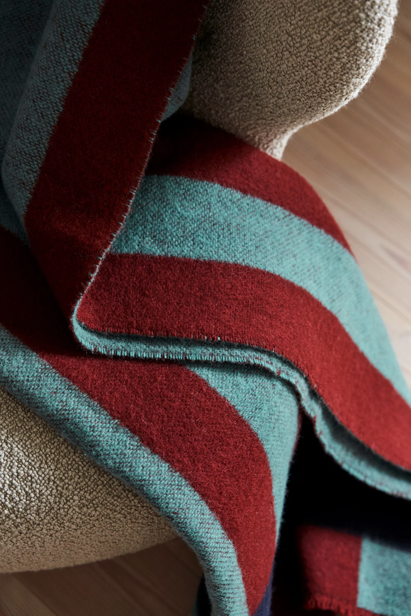 Folded striped blanket with dark red and teal bands draped over a textured light brown armchair.