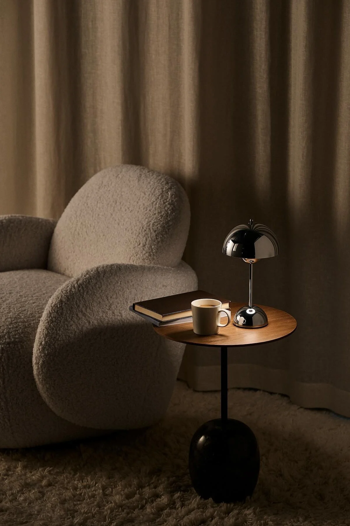 Next to the Mo armchair from 1898 stands a coffee table with a book, a cup of coffee and the chrome Flowerpot table lamp from &Tradition.