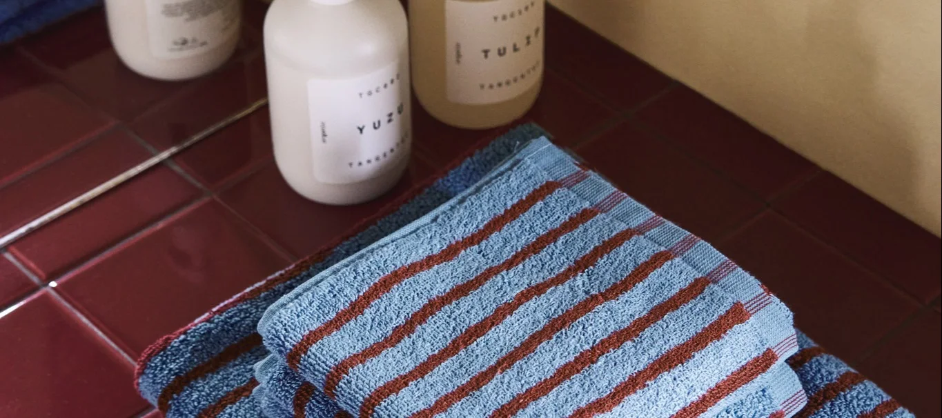 One of the interiors trends for autumn 2025 is patterns such as stripes and checks. Here, the red and blue striped towels from the Drift collection by Scandi Living lie on a red-tiled shelf.