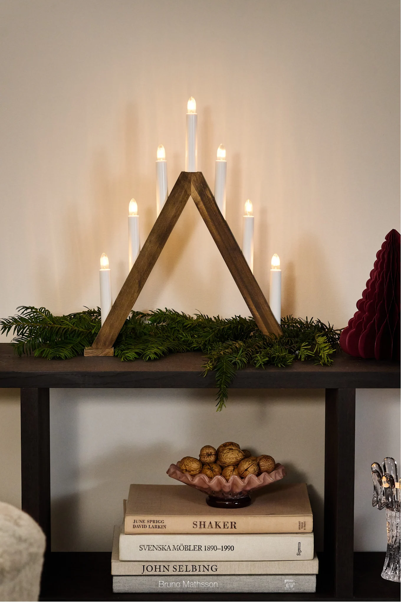 Minimalist Christmas decor. Here you see an electric candle arch in dark wood on a side board with a pink bowl full of walnuts.
