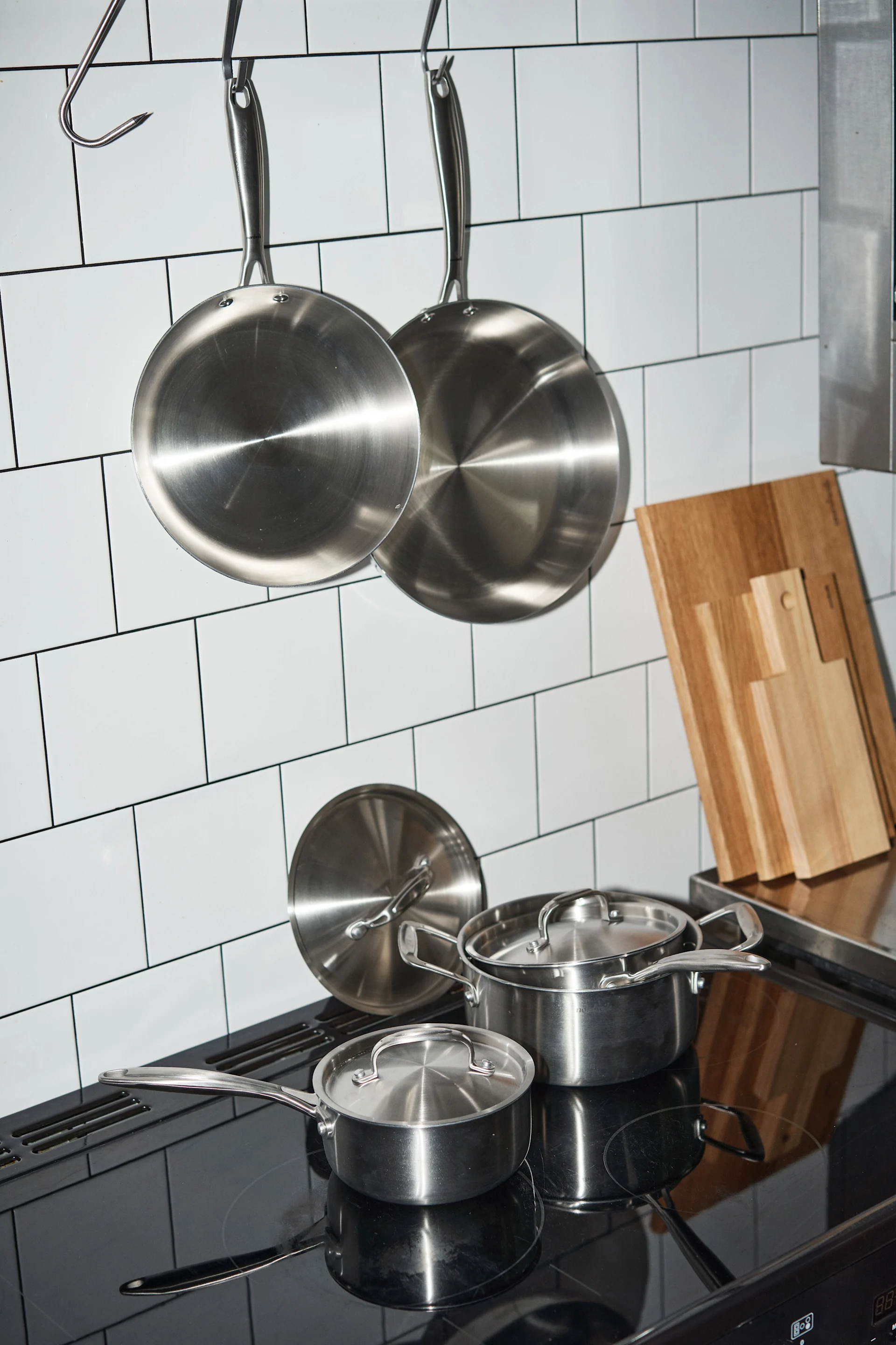 Clean pans from Nordwik hang in a tiled kitchen, with pots from Nordwik on the hob below.