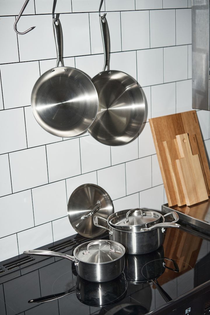 Clean pans from Nordwik hang in a tiled kitchen, with pots from Nordwik on the hob below.