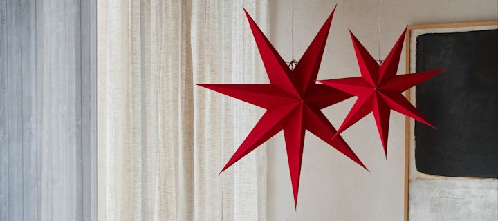 Two red paper star lanterns from Watt & Veke hanging in a living room setting. 