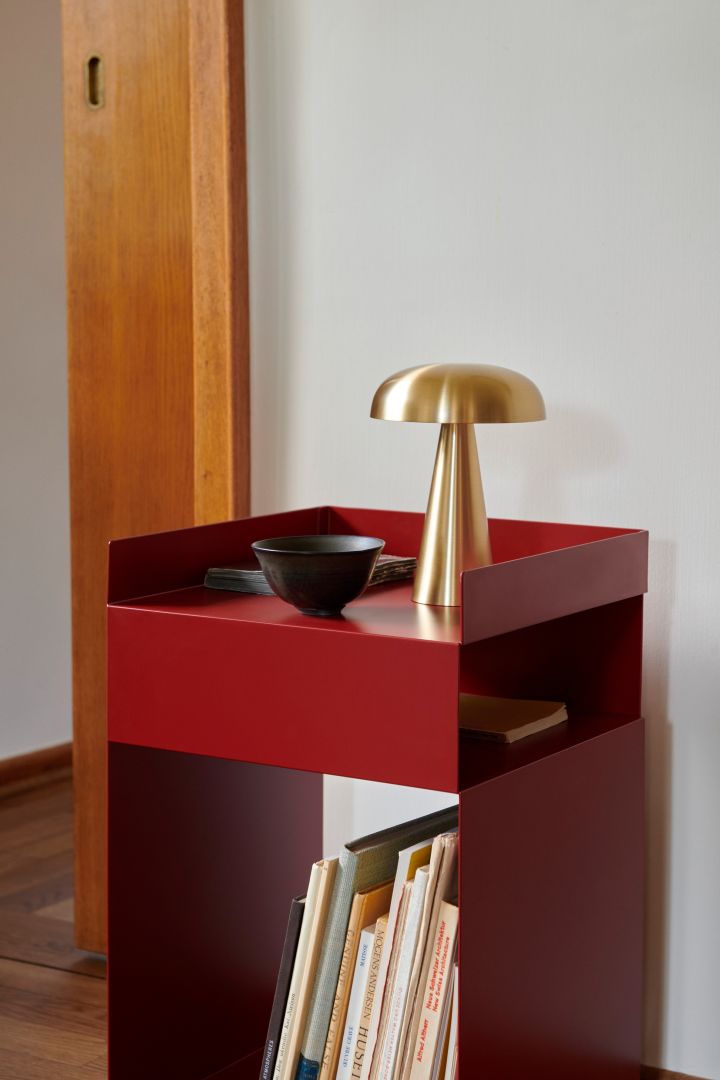 Red furniture and interior details are big in the 2024 Scandinavian interior design trends and are seen here at &Tradition in the form of a red side table with a small brass lamp on it.  