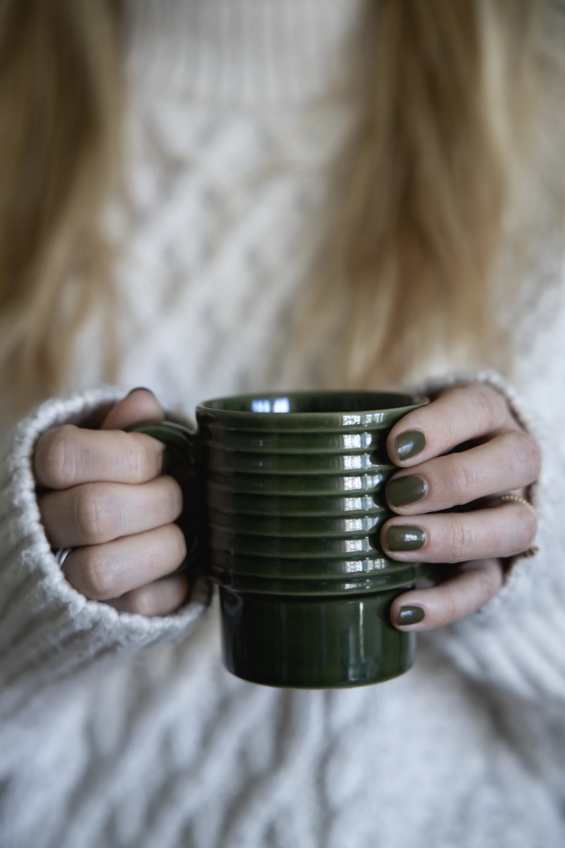 A woman in a white jumper holds a green mug from Sagaform's Coffee & more collection in her hands.