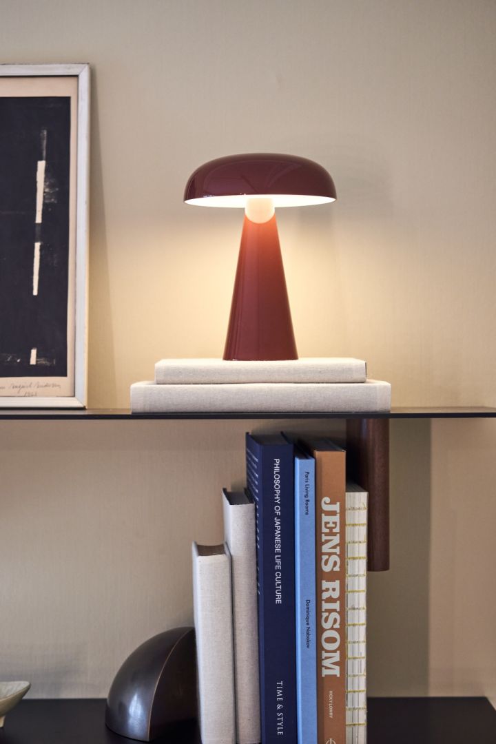 The cordless table lamp Como from &tradition sits on a shelf with books and a picture frame. 