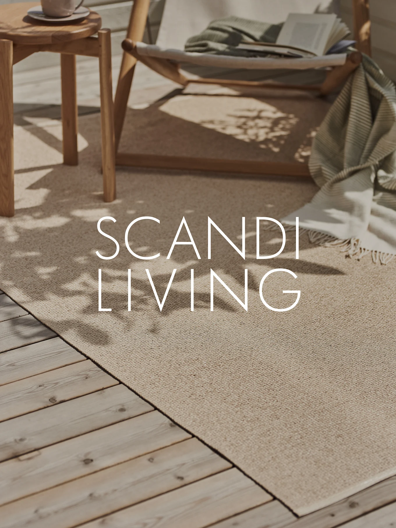 A light beige outdoor rug on a wooden deck with a lounge chair, a blanket, a book, and a side table with a cup. Overlay text: SCANDI LIVING.