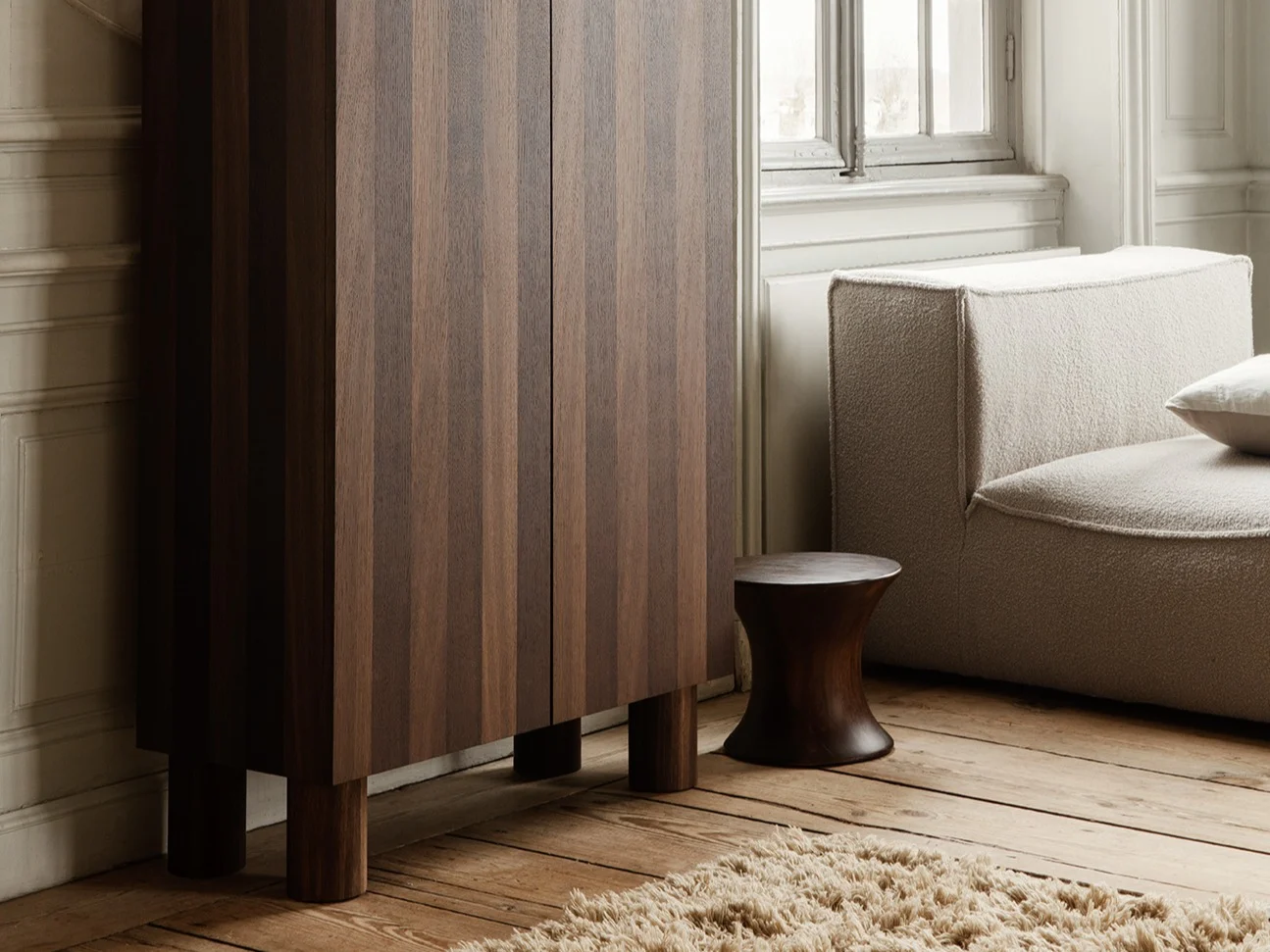 Elegant room with dark wood fluted cabinet, sculpture of kneeling woman, light modular sofa, and large window.