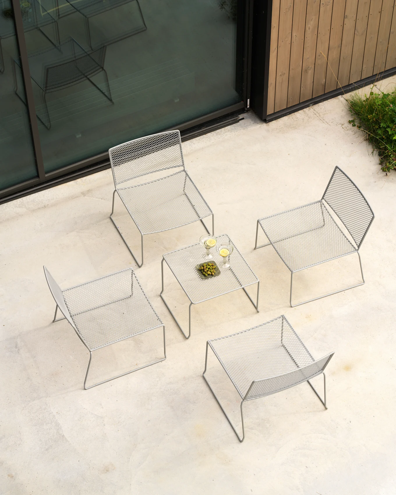 Overhead view of a light gray outdoor lounge set with four mesh chairs and a table with drinks and olives on a concrete patio.
