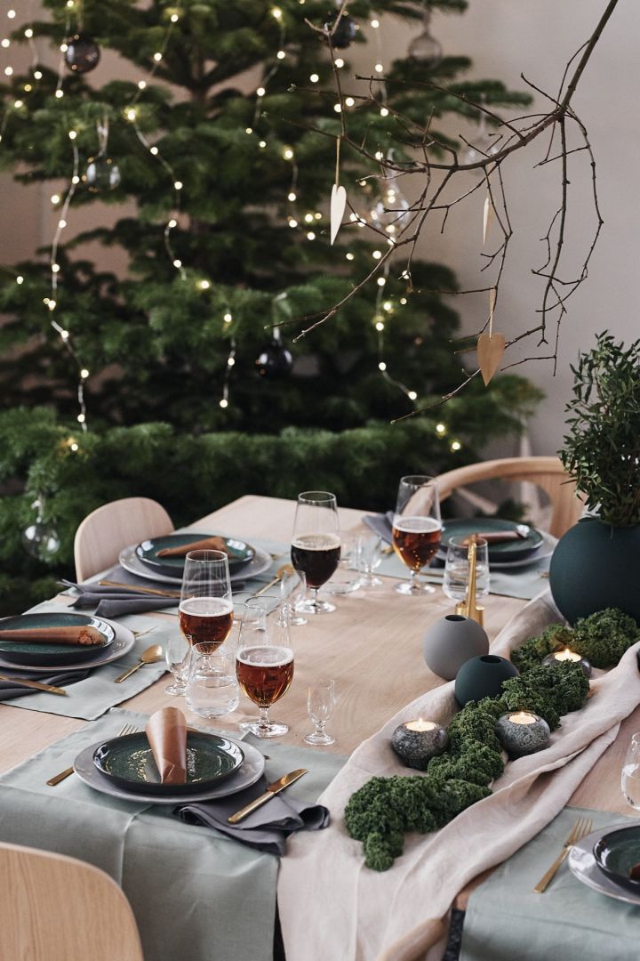 The table is set up for Christmas dinner with a green decoration with green plates, gold cutlery and green vases.