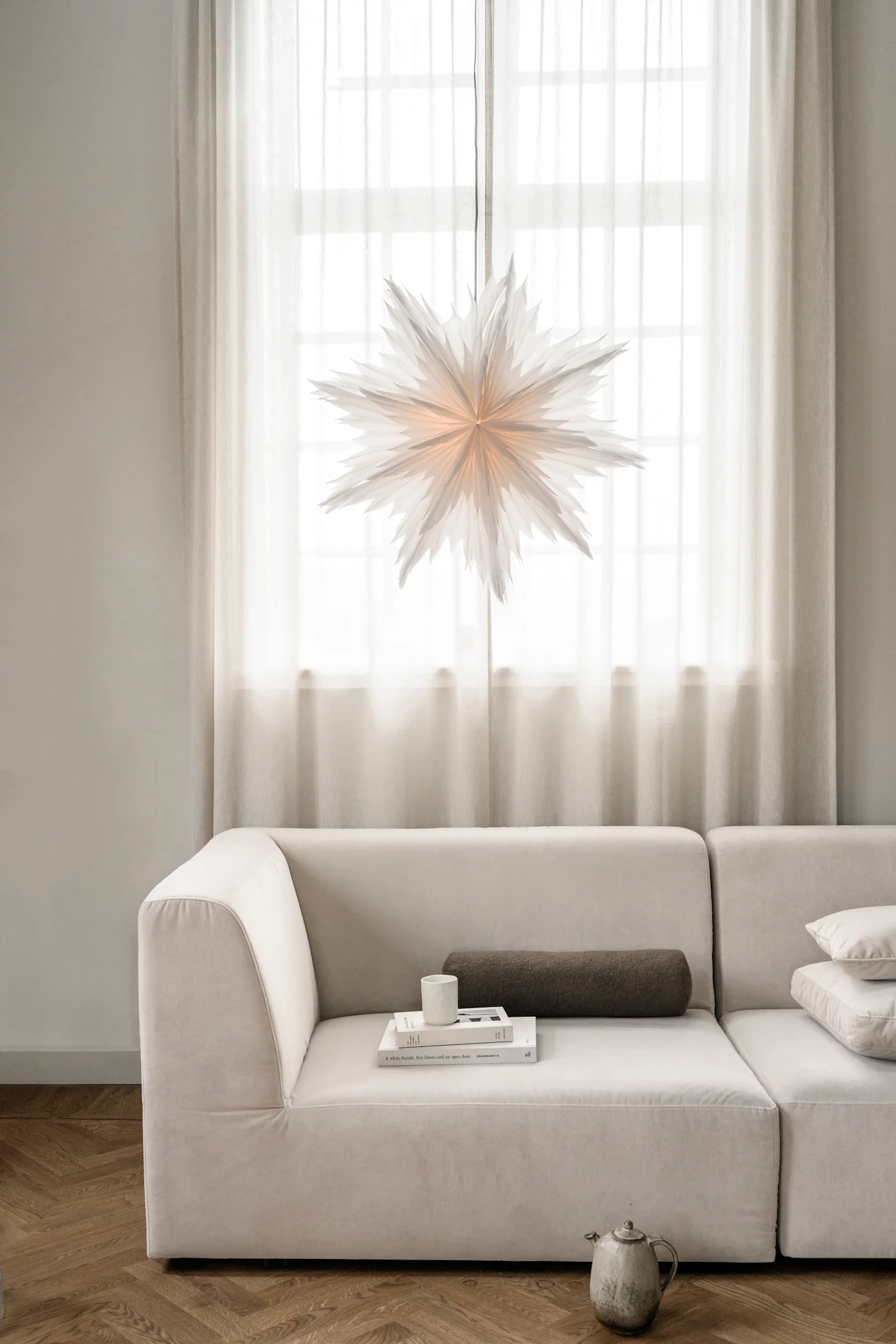Minimalist Christmas decor like the Oslo paper Christmas star from Watt & Veke. Seen here hanging in the window of a neutral coloured living room. 