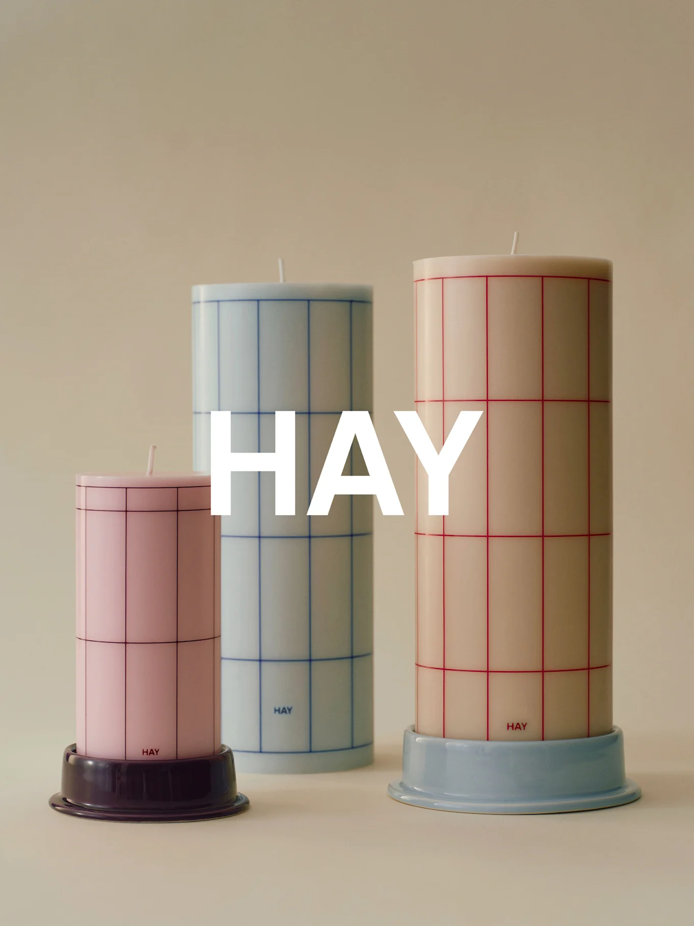 Three grid-patterned cylindrical candles of varying heights: pink, light blue, and cream, on bases.