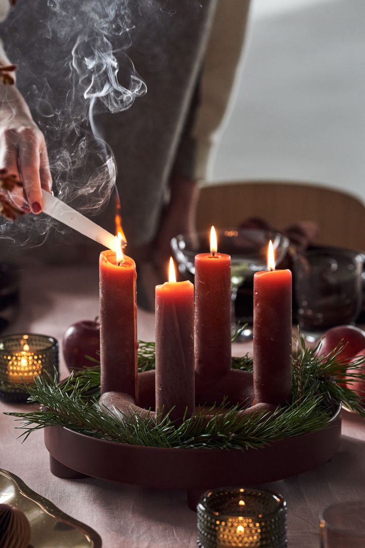 The Lucia Advent candle from Broste Copenhagen on a red tray from Muuto, surrounded by some small branches from a Christmas tree. One of the most stylish Christmas decorations for 2021. 
