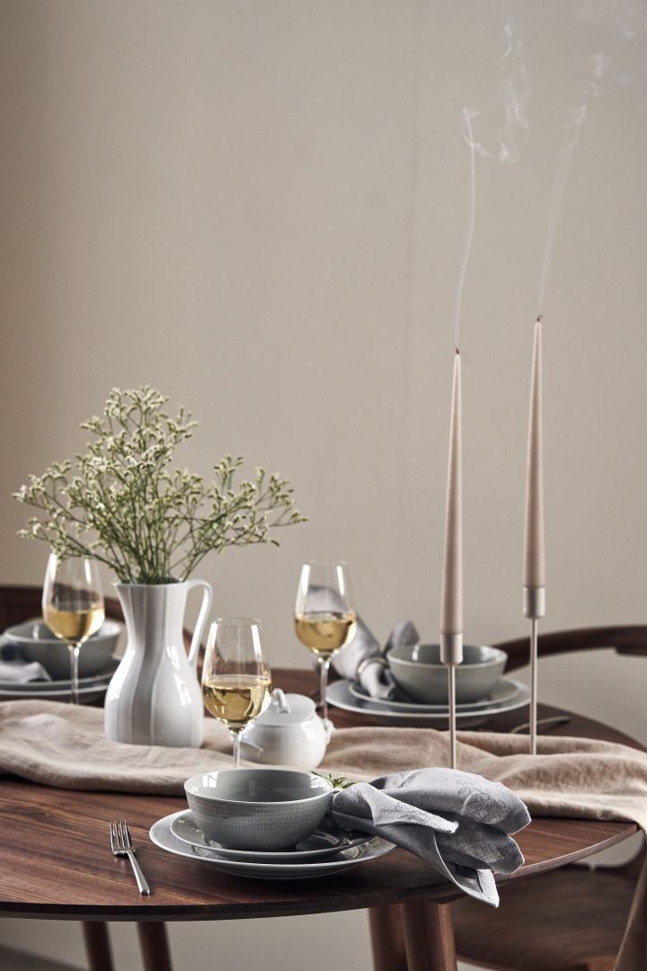 A festively set table with candles, meadow flowers in a carafe by Pli Blanc and Swedish Grace porcelain in white and grey. 