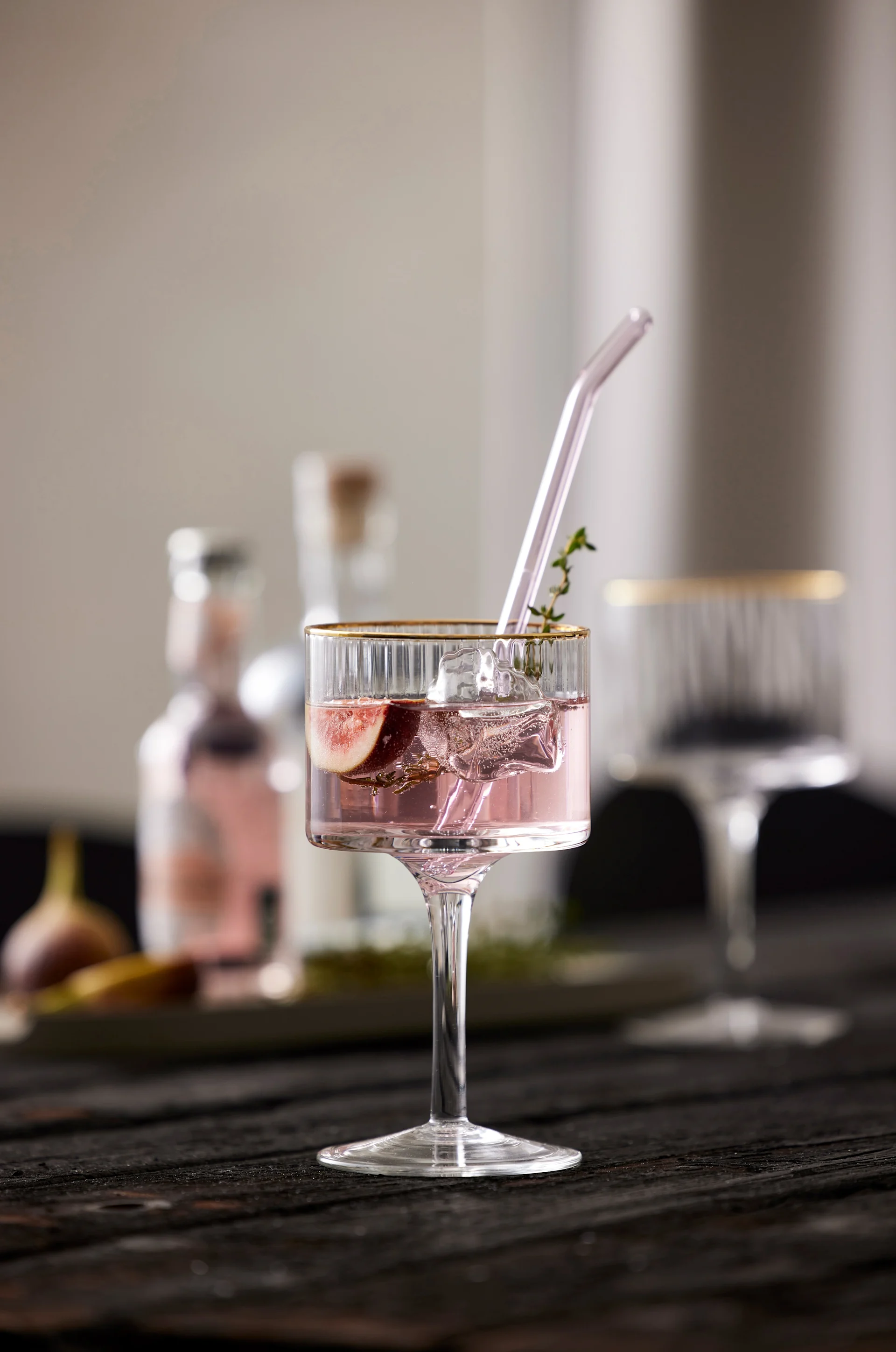 A purple mocktail with a glass straw and decorated with thyme stands on a table, served in a Palermo Gold Gin & Tonic glass from Lyngby Glas.