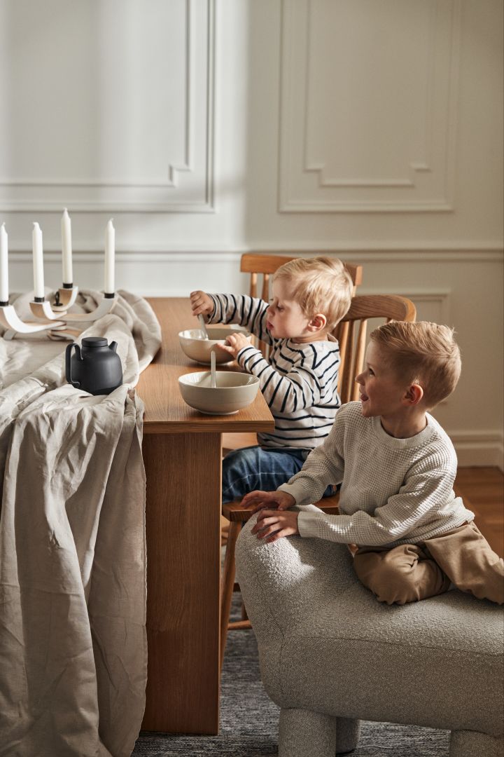 Two boys are sitting at a dinner table from Design House Stockholm, the picture also shows the Lulu pouf and bowls from the NM&Sand series.