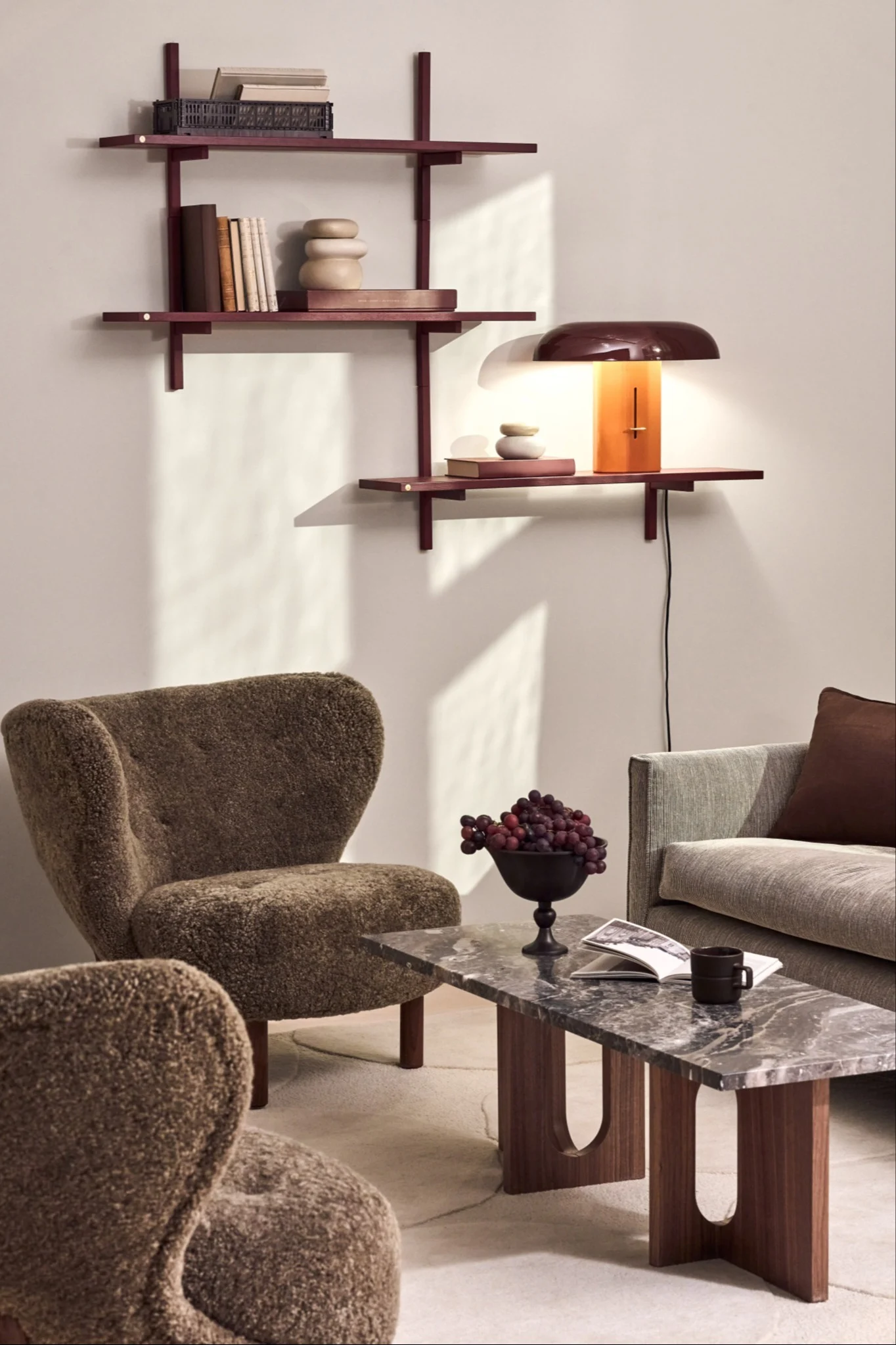 A living room with two armchairs, a sofa, and a stone table, where a lamp illuminates the shelf and small details on the table and shelf reflect the interior design trends of 2026