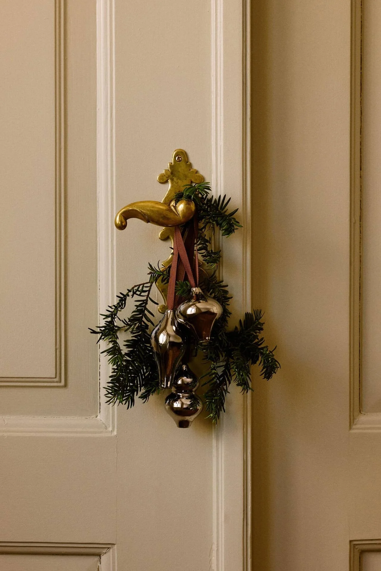 Brass door handle decorated with green pine branches and three shiny silver mercury glass ornaments.