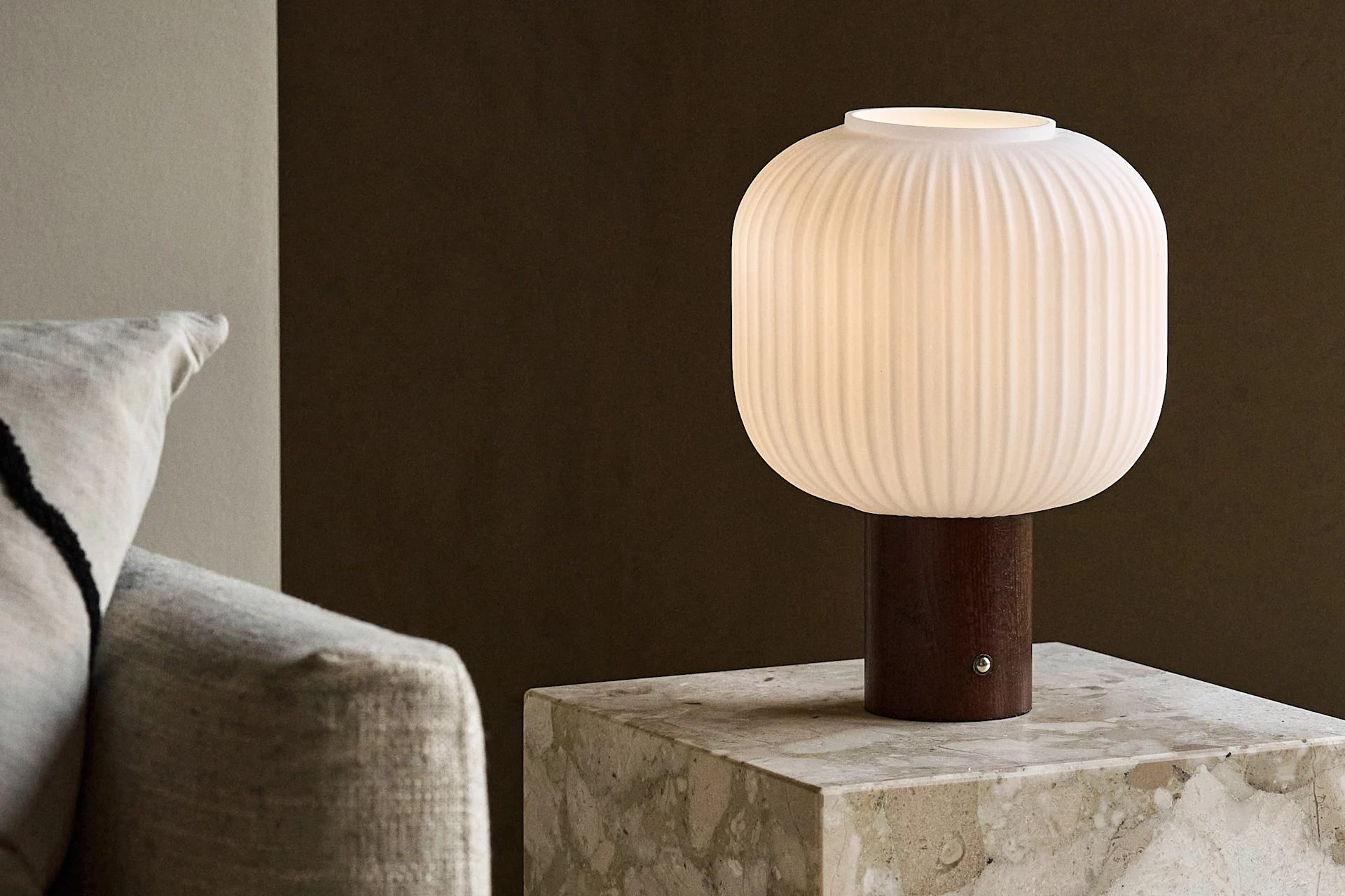 White ribbed table lamp with a wooden base on a marble side table next to a sofa.