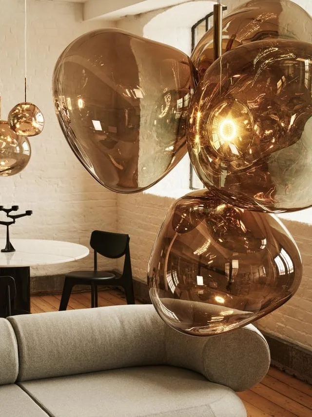 A modern living room with a curved grey sofa, a matching ottoman with magazines, and amber glass pendant lights.
