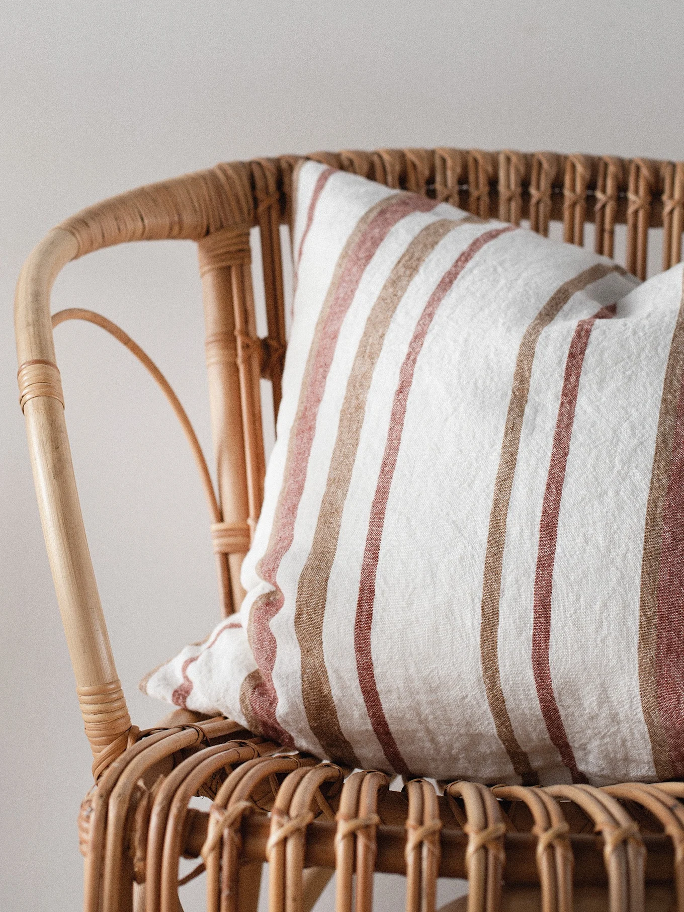 Close-up of a natural rattan chair with a white cushion featuring vertical light brown and muted reddish-brown stripes.